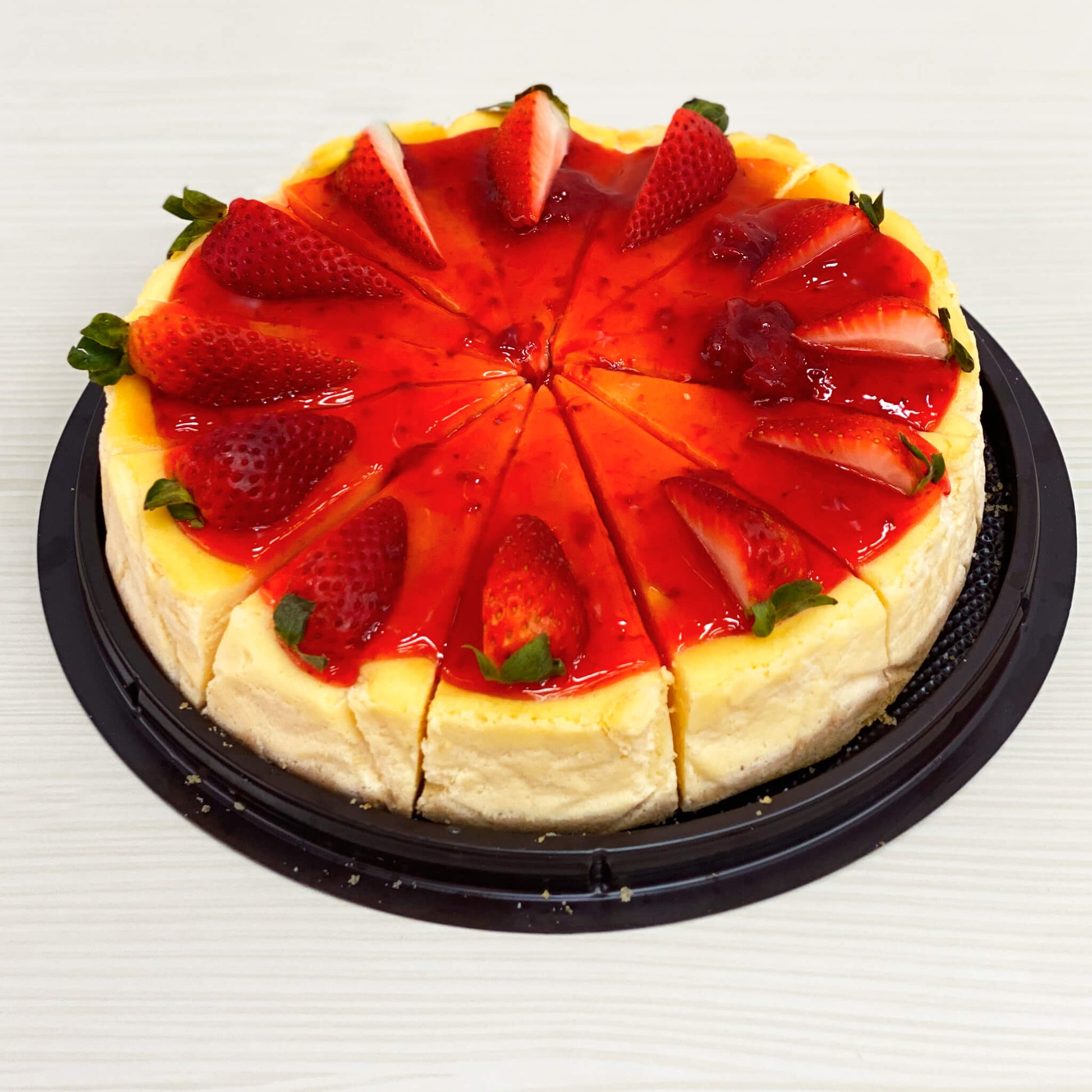 ชีสเค้กสตรอเบอร์รี่ทั้งก้อน หั่นเป็นชิ้น โรยหน้าด้วยซอสสตรอเบอร์รี่และสตรอเบอร์รี่สดบนถาดสีดำ