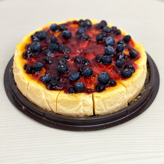 ชีสเค้กบลูเบอร์รี่ทั้งก้อน หั่นเป็นชิ้น โรยหน้าด้วยซอสบลูเบอร์รี่เข้มข้นและผลบลูเบอร์รี่สดบนถาดสีดำ