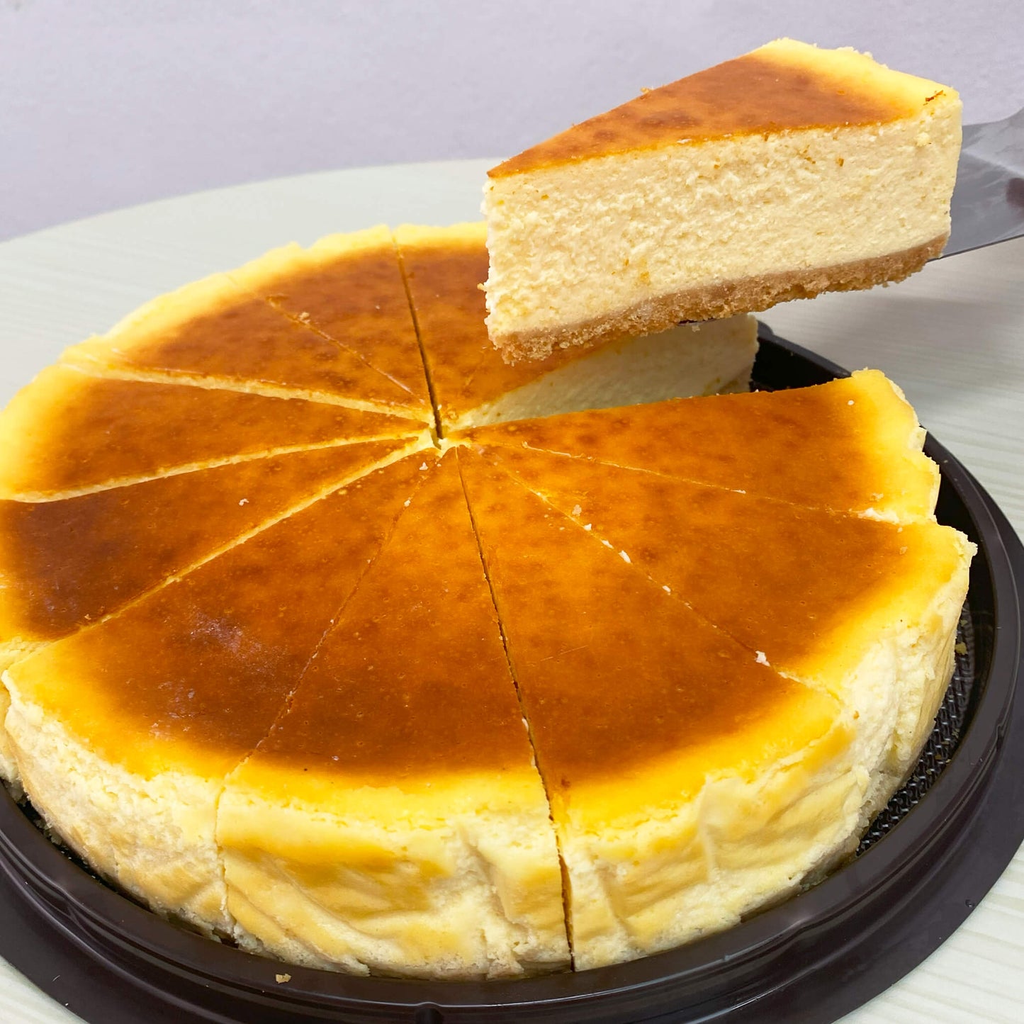 ชีสเค้กคลาสสิกทั้งก้อน หั่นเป็น 12 ชิ้น พร้อมเสิร์ฟบนถาดสีดำ